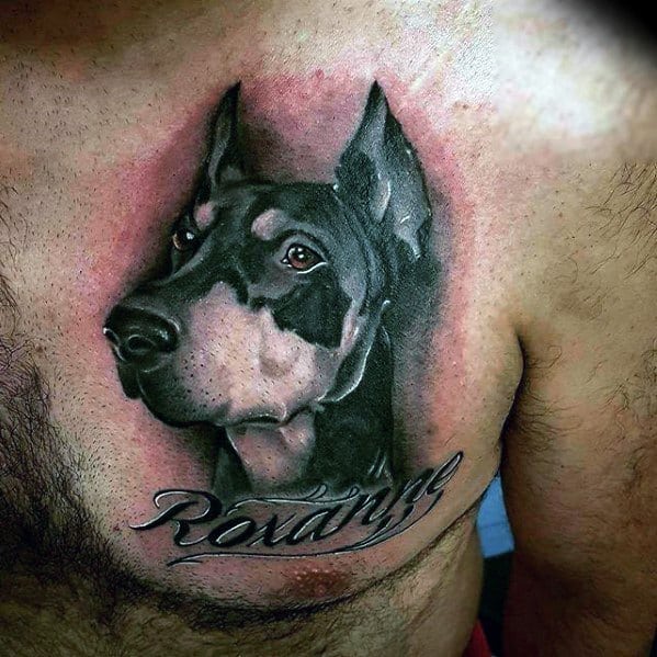 Realistic Doberman chest tattoo with soft shading and the name “Roxanne” scripted below, capturing a loyal and personal tribute.