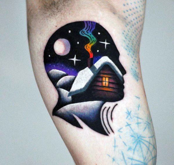 Colorful tattoo of a head silhouette filled with a snowy cabin scene, glowing window, starry sky, and rainbow smoke rising into the night.