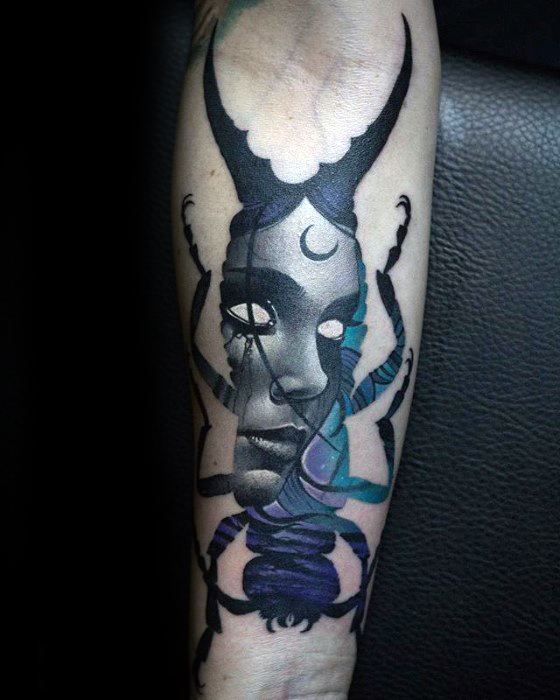 Dark surreal tattoo of a woman’s face with glowing eyes and horns, blended into a beetle body with celestial and mystical elements.