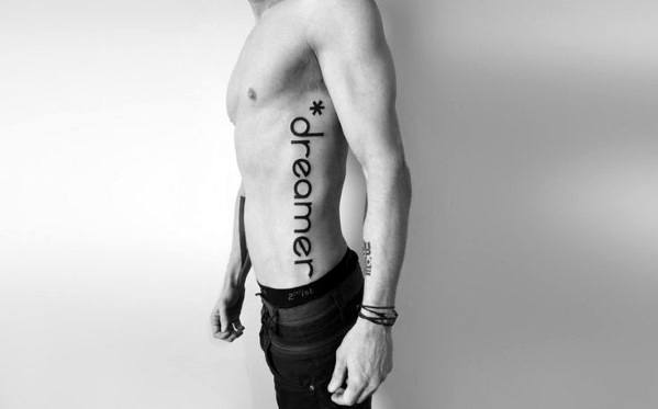 Large vertical side tattoo with the word “*dreamer” in bold, modern font running down the torso from ribs to hip.