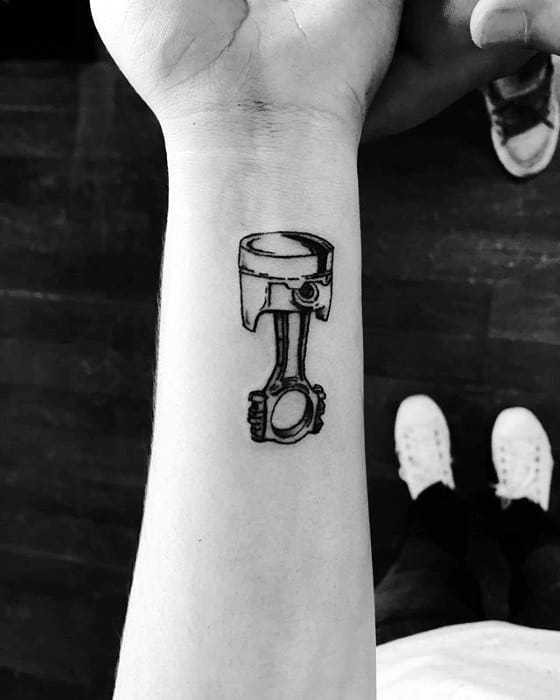 Tattoo of a realistic engine piston and connecting rod, inked in bold black lines on the inner forearm, symbolizing power and mechanics.