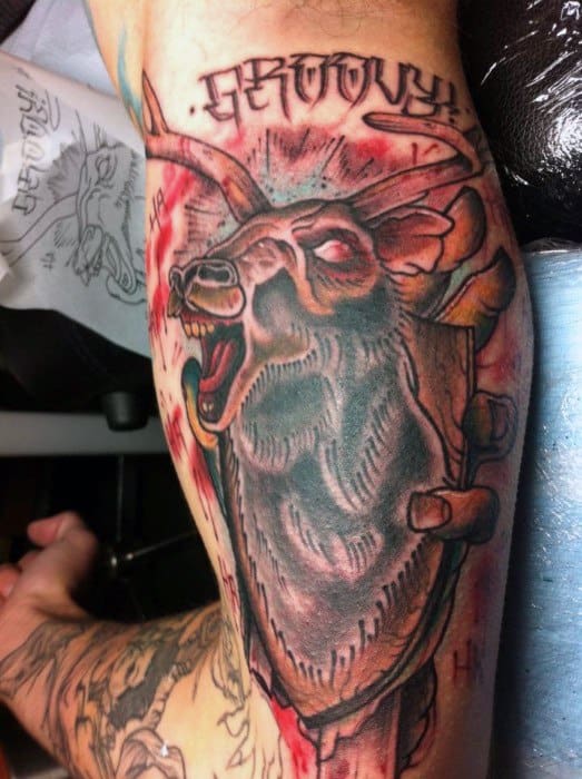 Evil Dead tattoo of the mounted deer head laughing maniacally with glowing eyes, red highlights, and “Groovy” written above in stylized text