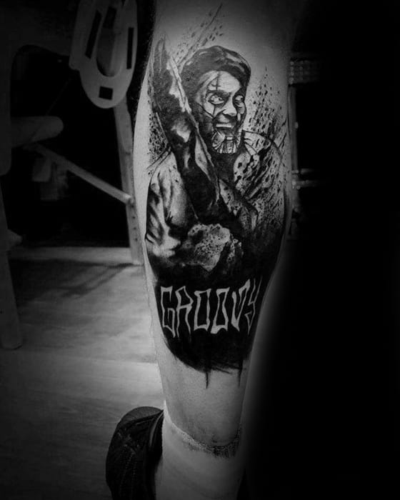 Black and white Evil Dead tattoo of Ash holding his chainsaw with splatter effect and bold “Groovy” text below in a gritty horror style.