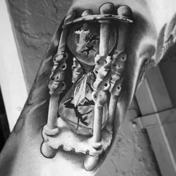Hyper-realistic tattoo of an hourglass with tiny falling figures inside, symbolizing time slipping away, inked on the upper arm.