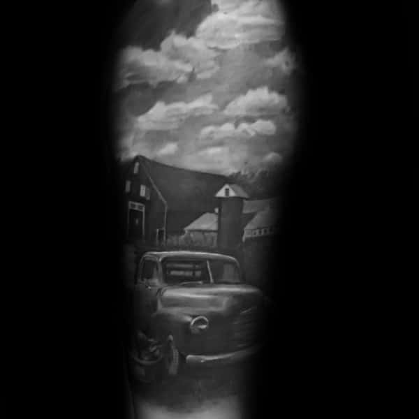 Black and gray tattoo of a vintage truck parked in front of a barn with a cloudy sky, creating a nostalgic rural scene.