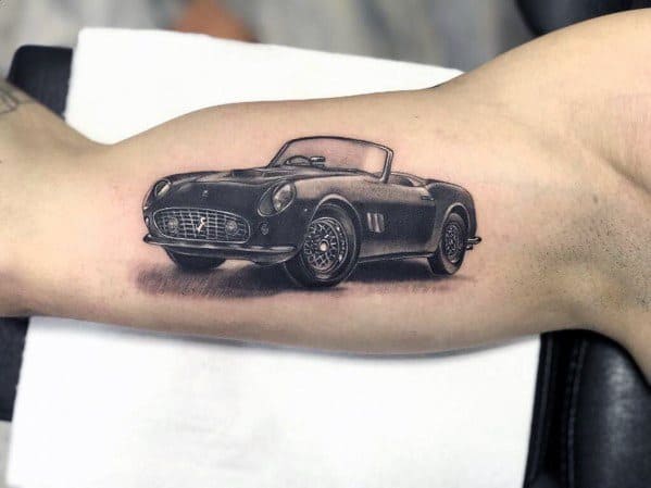 Classic black-and-grey Ferrari convertible tattoo on man's inner arm, capturing vintage charm and automotive elegance.