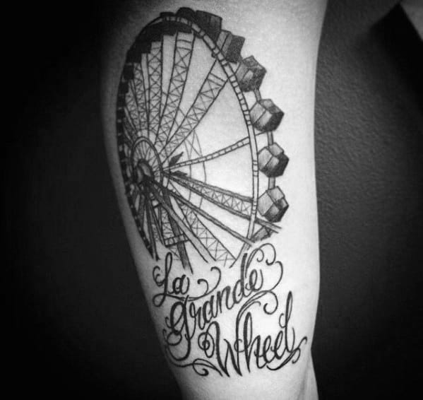Realistic black and grey Ferris wheel tattoo with bold shading and intricate details, featuring elegant script that reads "La Grande Wheel."