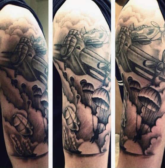 Tattoo of WWII airplanes and paratroopers on a person's upper arm in black and gray ink