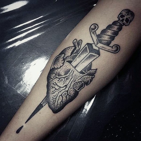 Tattoo of a dagger piercing an anatomical heart on an arm, with a small drop of blood