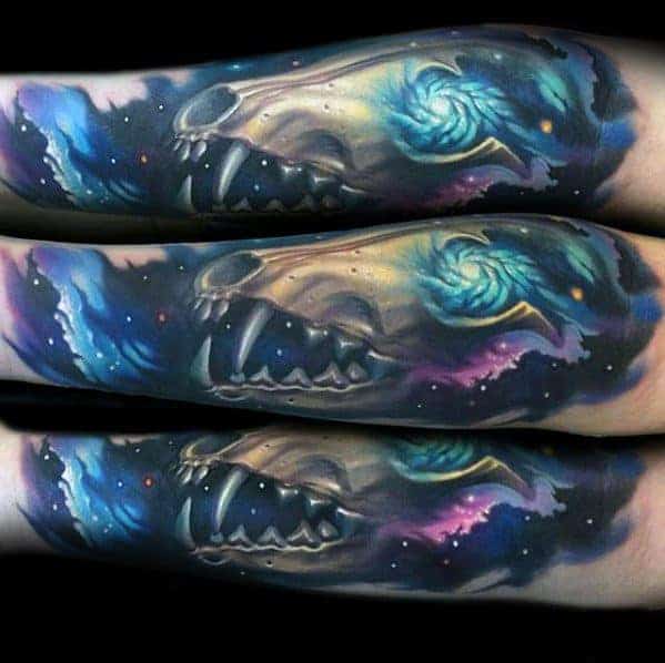 Tattoo of a wolf's skull with a colorful cosmic background on someone's forearm