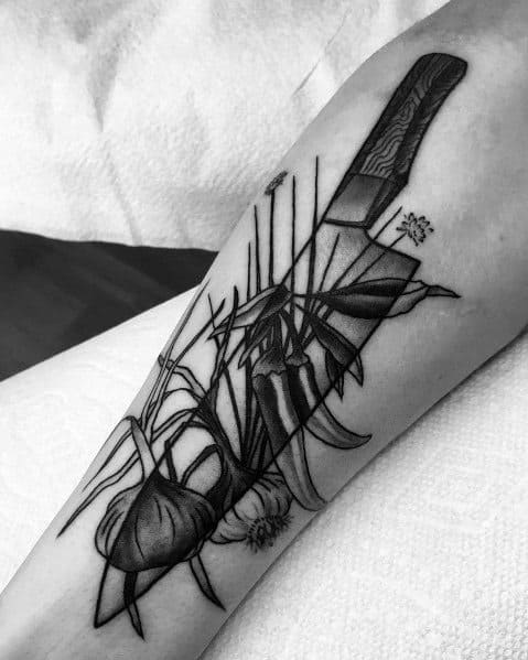 Black and grey garlic and knife tattoo with bold shading and fine line details, creating a sharp and dynamic culinary-inspired design.