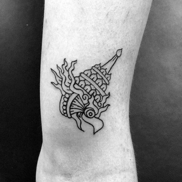 Minimal Garuda tattoo on the leg featuring a bold black outline of a stylized head with a crown and flame-like accents.