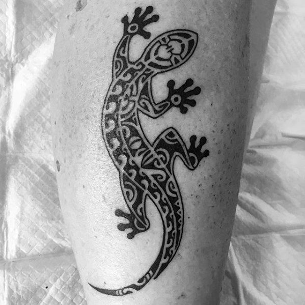 Bold tribal gecko tattoo with intricate black line patterns, positioned on the leg in a climbing stance.