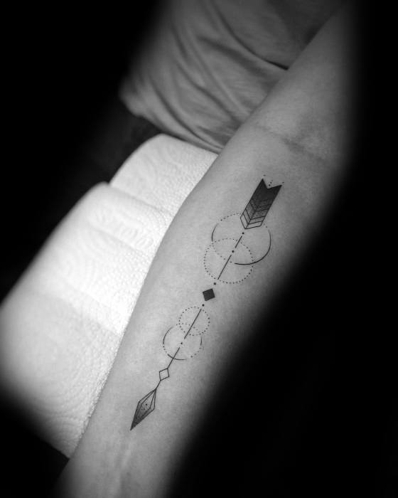 Simple geometric arrow tattoo with dotted circles, diamonds, and clean linework running along the forearm.