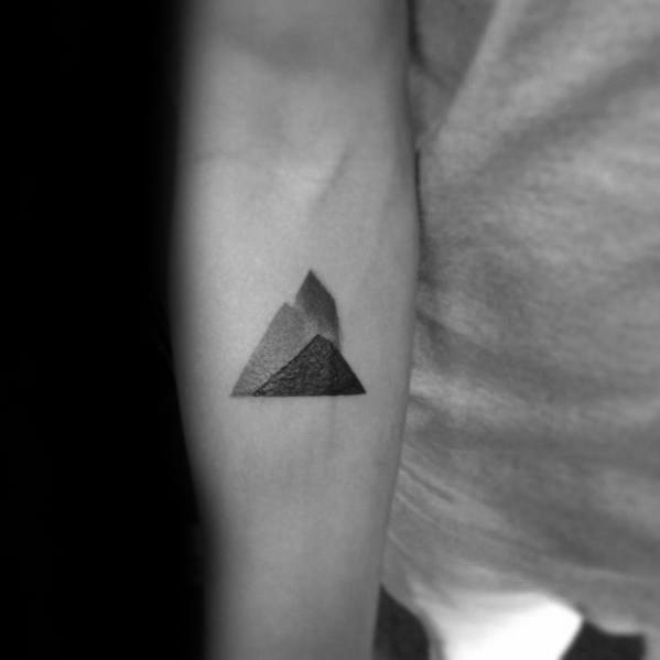Minimalist mountain tattoo with three overlapping shaded triangles forming abstract peaks on the inner forearm.