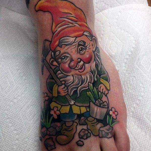 Tattoo of a cheerful gnome with a red-orange hat, holding a pickaxe and a bucket of plants, standing among flowers and rocks.