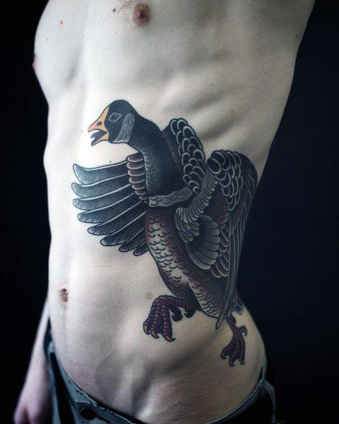 Bold traditional-style tattoo of a dark-feathered goose with outstretched wings, inked on the ribcage with rich shading and intricate details.