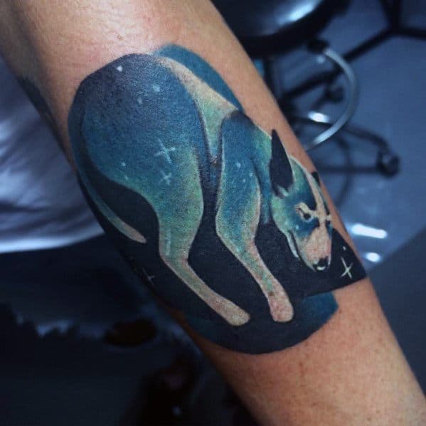 Gradient tattoo of a stylized dog in shades of blue, green, and beige with white stars, set against a black geometric background.