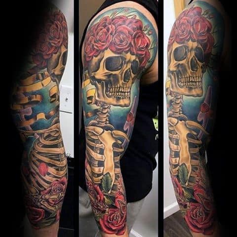 Vibrant Grateful Dead sleeve tattoo of a skeleton with red rose crown and detailed ribs, blending blue sky and floral elements.