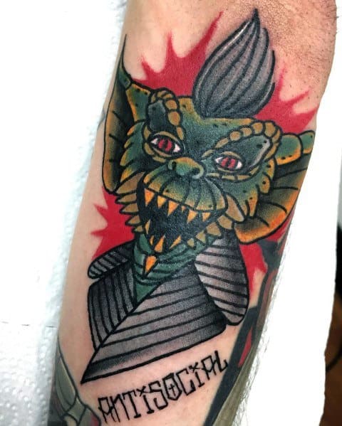 Bold Gremlin tattoo with a mohawk, sharp teeth, and red eyes, featuring a comic-style design with 'Antisocial' text for an edgy look.