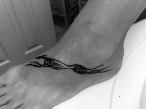 A minimalistic black tattoo of two stylized greyhounds in motion, designed to wrap elegantly along the foot with swirling accents.