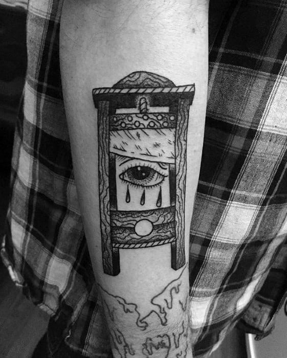 Surreal blackwork guillotine tattoo featuring a single eye with teardrops on the blade and detailed wood texture throughout.