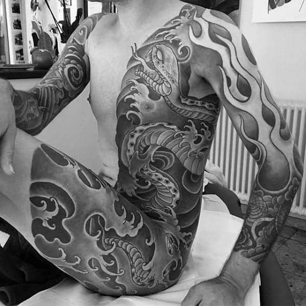Japanese half-body tattoo featuring a coiled snake, bold flames, and dynamic waves in shaded black and grey tones