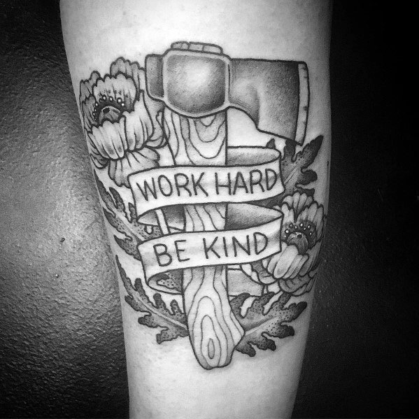 Black and grey hatchet tattoo with a wood-textured handle, floral details, and a ribbon wrapped around it displaying "Work Hard Be Kind."