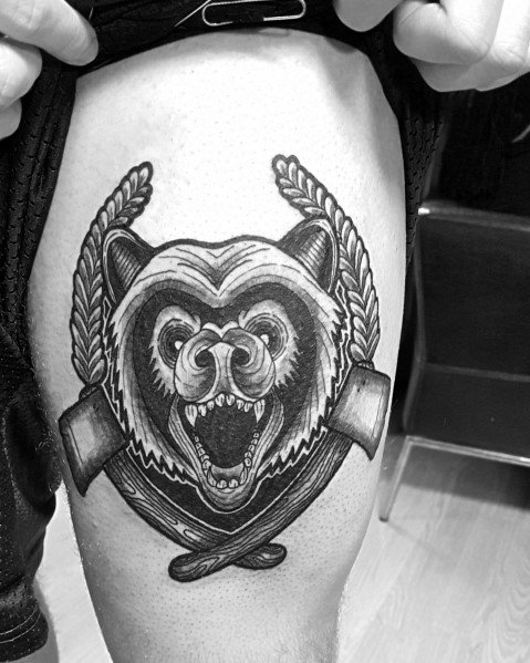 Bold black and grey tattoo of a roaring bear with crossed hatchets and braided rope details, inked on the upper thigh for a fierce look.