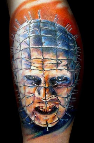 Realistic *Hellraiser* tattoo of Pinhead with intense blue and orange hues, detailed facial shading, and piercing pins for a vivid, chilling look.