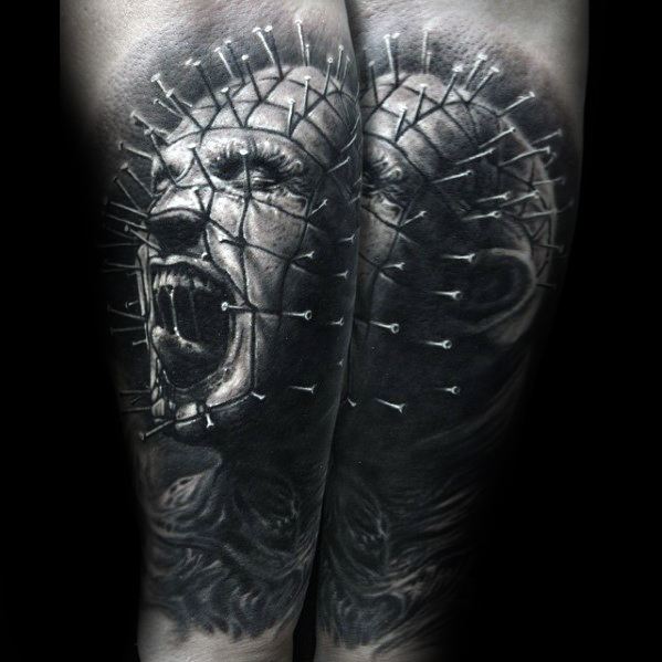 Hyper-realistic black and grey *Hellraiser* tattoo of Pinhead, featuring intense shading, dual perspectives, and intricate pin details for a haunting effect.