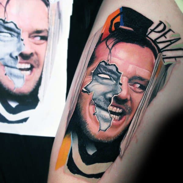 Creative color tattoo of Jack Torrance from *The Shining*, featuring a split-face design with a cracked mask effect and bold artistic elements.