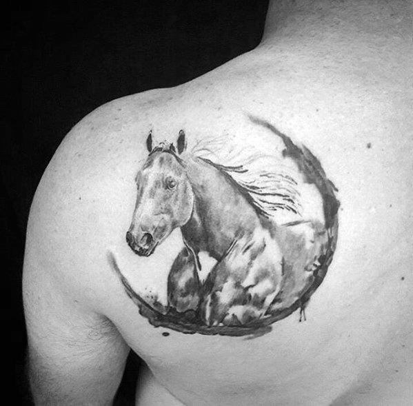 Watercolor-style black and grey tattoo of a horse in motion with a brushstroke circle, placed on the upper shoulder blade