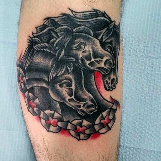 Neo-traditional tattoo of three black horse heads with bold lines, red accents, and floral pattern wrapping around the design