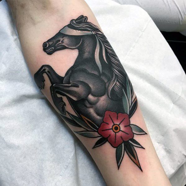 Traditional-style tattoo of a rearing black horse with a flowing mane, red flower, and bold leaves on the forearm