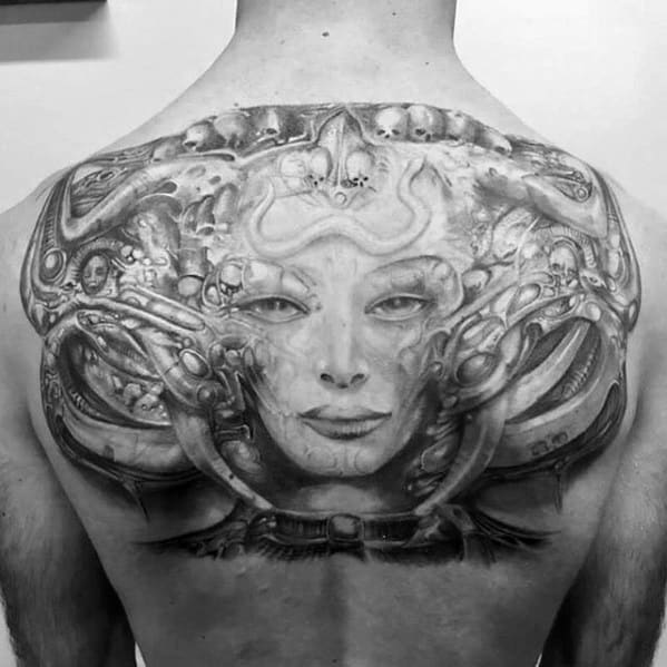 HR Giger-inspired chest tattoo featuring a surreal biomechanical female face surrounded by alien skulls, tubes, and mechanical forms.