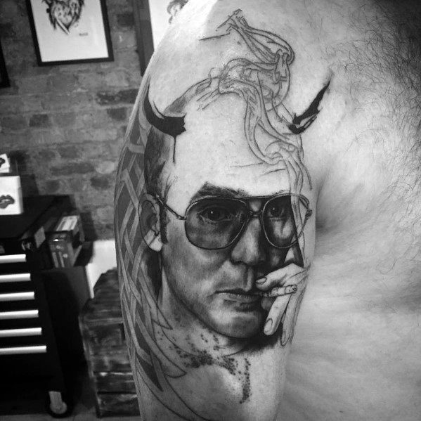 Black and white Hunter S. Thompson tattoo featuring a realistic portrait with aviator glasses, a cigarette, devil horns, and smoke morphing into surreal shapes.