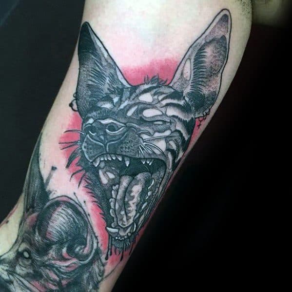 Black and grey hyena tattoo with bold linework and shading, featuring a snarling face and red background for dramatic contrast.