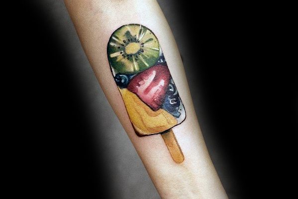 Vibrant tattoo of a fruit popsicle featuring realistic kiwi, strawberry, mango, and blueberry details, blending bright colors with smooth shading.