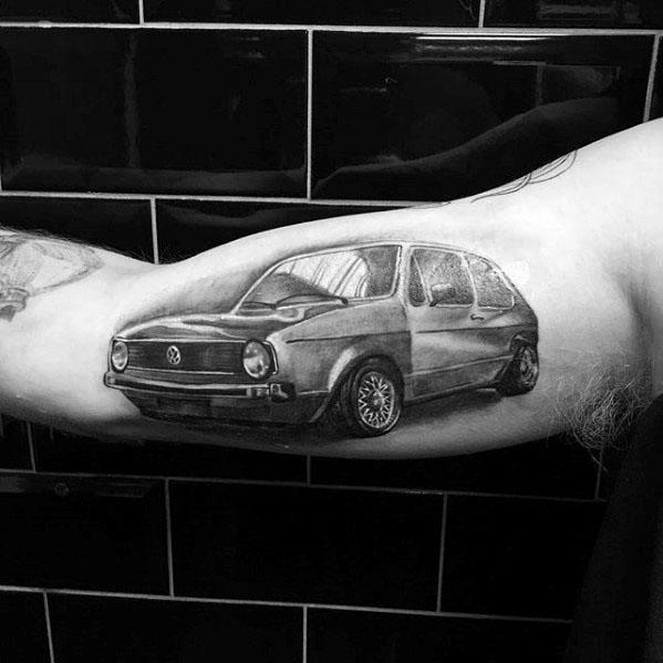 Black and gray tattoo of a classic Volkswagen Golf on the inner bicep, detailed with realistic shading and perspective.