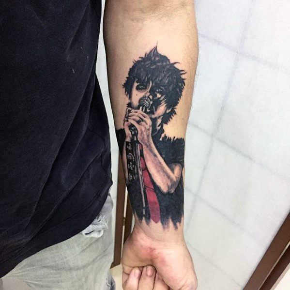 Forearm tattoo of Billie Joe Armstrong singing into a mic, with dark tones and red highlights capturing his intense stage presence.