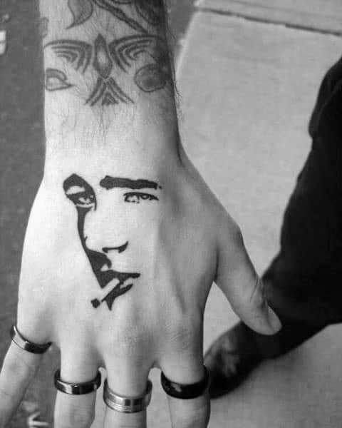 Minimalist James Dean face tattoo in bold black ink on the hand, with abstract negative space and cigarette detail.
