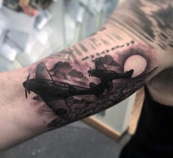 Tattoo of airplanes flying towards a sunset on a person's arm with clouds in the background