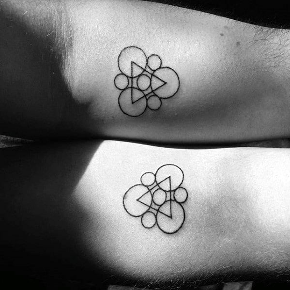 Matching minimalist Keywork tattoos with fine black lines, symbolizing Coheed and Cambria’s logo on both inner arms.