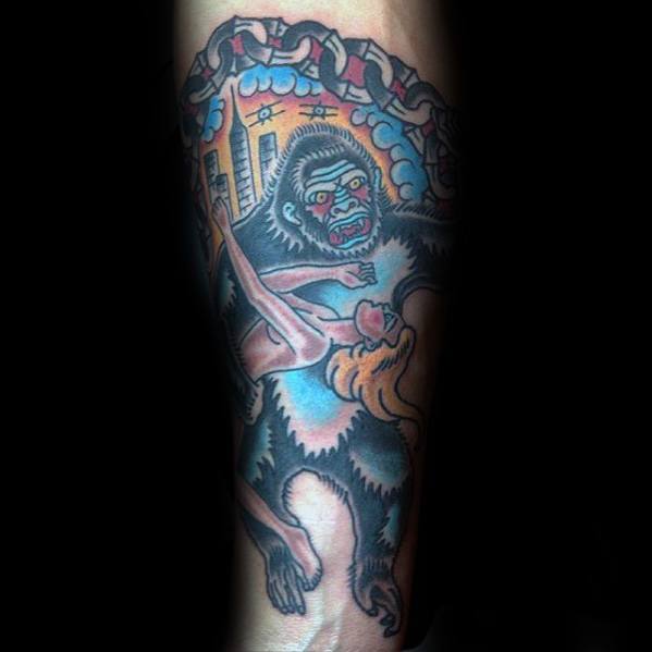 Traditional style King Kong tattoo in bold colors, showing Kong holding a woman with a cityscape and broken chains in the background.