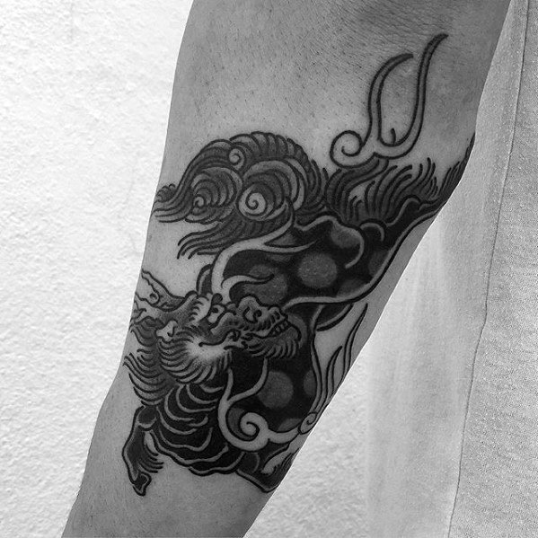 Forearm Kirin tattoo in bold black ink with flowing clouds, fierce expression, and strong contrast for a striking traditional look.