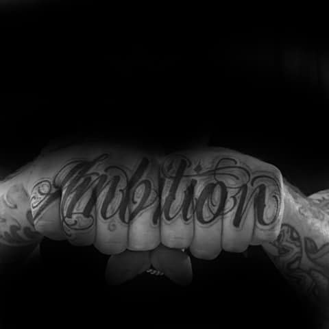 Tattooed knuckles boldly spell "Ambition" in striking script font