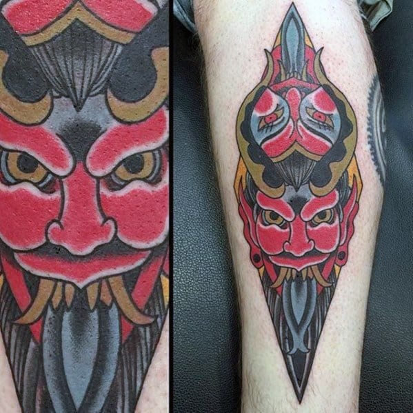 Geometric Krampus tattoo with bold red, black, and gold tones, featuring a symmetrical horned face and sharp pointed shapes.