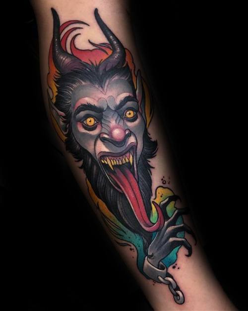 Vibrant Krampus tattoo on forearm featuring glowing yellow eyes, long red tongue, sharp claws, and a fiery multicolor background.