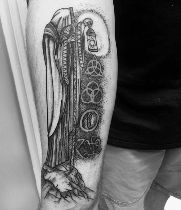 Forearm tattoo of the hooded hermit with a lantern above the four Led Zeppelin symbols, shaded with dotwork and rocky ground detail.
